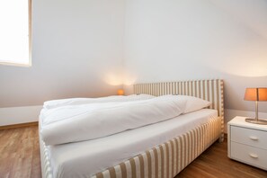 Una cama bien hecha con sábanas blancas, un cabecero a rayas y una lámpara de noche.