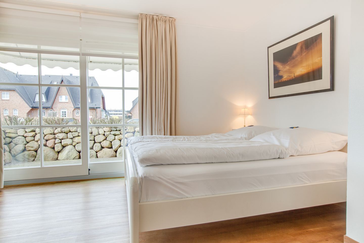 Une chambre avec une grande fenêtre, un lit et un tableau encadré accroché au mur.