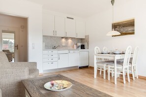 Una cocina moderna con armarios blancos, una zona de comedor con sillas blancas y una mesa de madera con una bandeja.