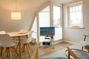 En moderne stue med spiseområde, store vinduer og et fladskærms-tv på et stativ.
