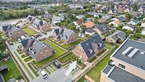 A residential area with detached houses, a parking lot, and a view of a cityscape in the background. - Sylter Quartier, Whg. 1 - In Zentraler und Dennoch Ruhiger Lage Westerlands Gelegenes 2-raum (Sylt)