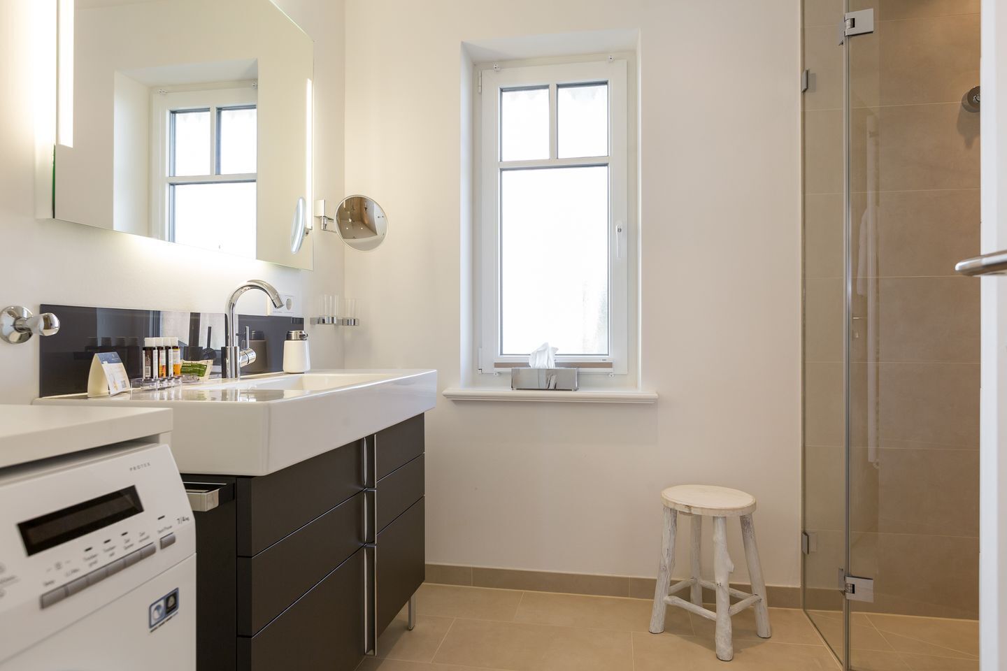 A modern bathroom with a large mirror, a sink, a window, and a shower area.