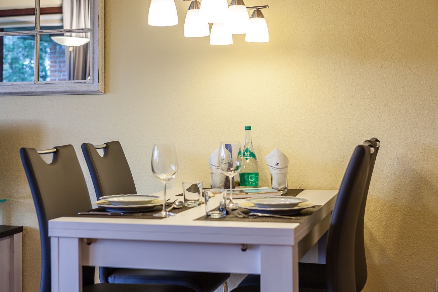 Une table à manger dressée avec des assiettes, des verres et une bouteille, entourée de chaises.