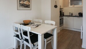 A dining area with a white table and chairs, a wooden bowl, and a framed picture on the wall. - Fortuna, App. 14 - Urlaub im Herzen Wenningstedts für bis zu 4 Personen (Wenningstedt-Braderup (Sylt))