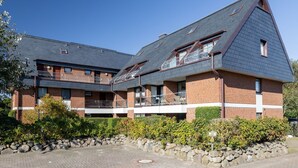A two-story building with a brick facade, multiple balconies, and a sloped roof. - Fortuna, App. 14 - Urlaub im Herzen Wenningstedts für bis zu 4 Personen (Wenningstedt-Braderup (Sylt))