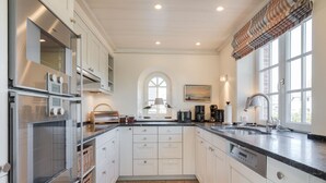 A modern kitchen with white cabinetry, a large window, and a view of the outdoors. - Haus am Strand, Beachfront - Strand, Meer & Luxus (Wenningstedt-Braderup (Sylt))
