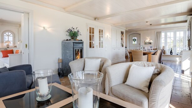 A spacious living room with a fireplace, a dining area, and a kitchen visible through an open door. - Haus am Strand, Beachfront - Strand, Meer & Luxus (Wenningstedt-Braderup (Sylt))