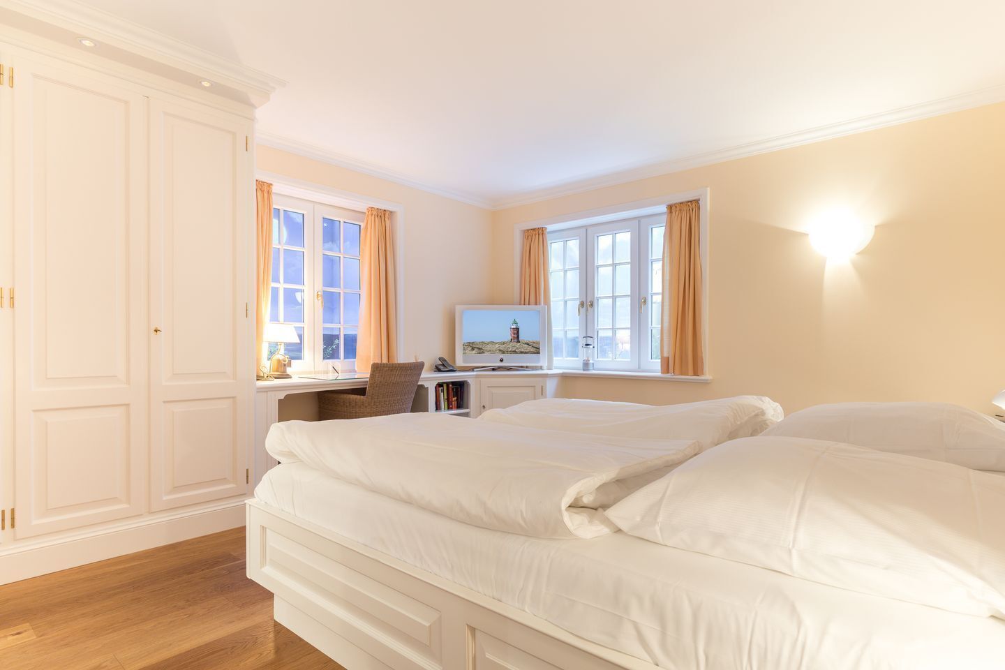 Quarto de hotel com uma cama grande, uma escrivaninha com um computador e uma televisão.