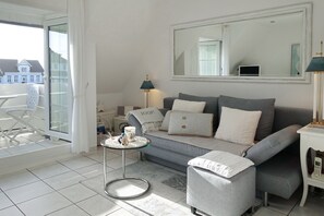 Un salón moderno con un sofá gris, una mesita auxiliar, una mesa redonda de centro y un espejo grande en la pared.