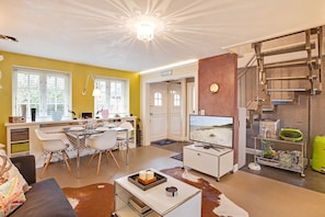 Una sala de estar moderna con comedor, televisor y escalera con barandilla de metal.