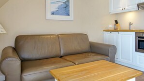 Ein gemütliches Wohnzimmer mit einem braunen Ledersofa, einem Holztisch und einer Küchenzeile mit weißen Schränken und einem eingebauten Ofen.