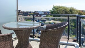 Ein Balkon mit Korbstühlen und einem Glastisch mit Blick auf einen Parkplatz und Wohnhäuser.
