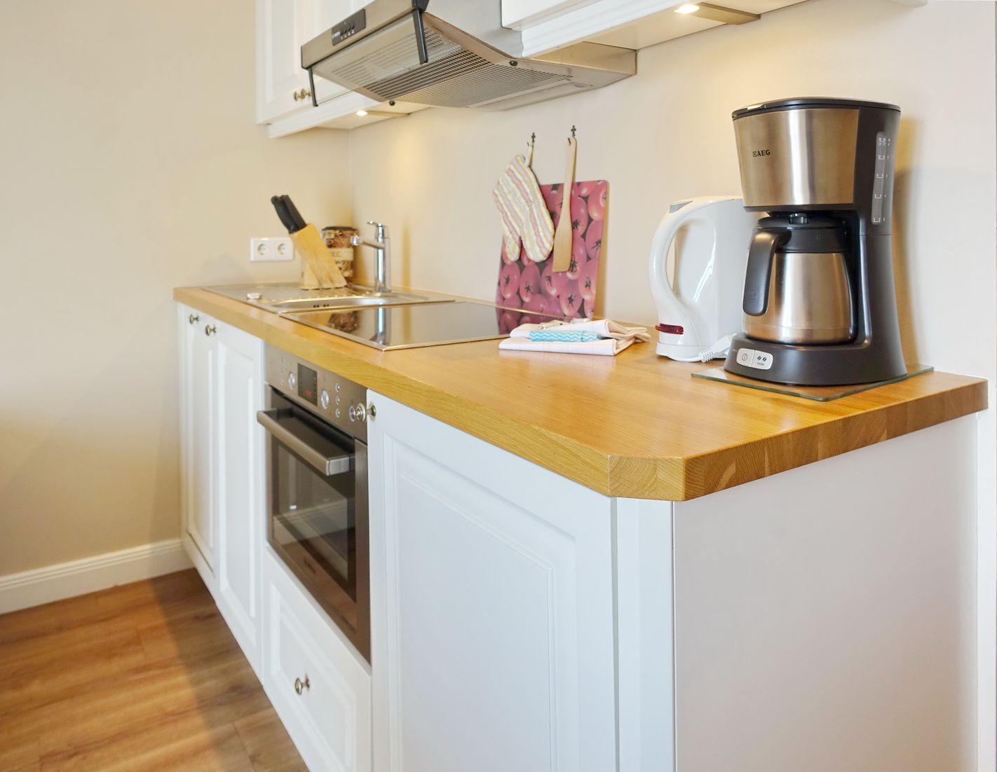 A kitchen with white cabinetry, a stainless steel coffee maker, and a wooden countertop.