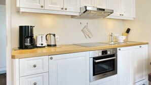 Une cuisine moderne avec des meubles blancs, un four Bosch, une machine à café, une bouilloire et un grille-pain.