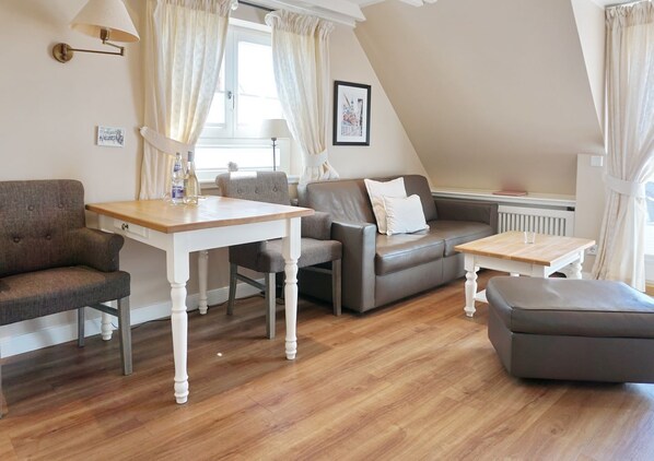 A cozy living room with a wooden table, a grey sofa, and a brown armchair.