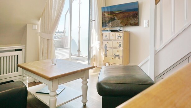 Une pièce avec une table en bois, un banc, un meuble orné de dessins d’animaux et un tableau représentant un paysage.