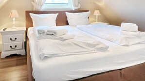 Un lit jumeau bien fait, avec du linge de lit blanc, deux tables de chevet avec des lampes et une fenêtre avec des rideaux.