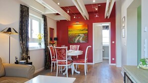 A modern living room with a dining area, featuring a red accent wall, a painting, and a view into the dining room. - Haus Silvana, App. 6 - 2-raum Appartement mit ca. 50m ² Nutzfläche im Obergeschoss (Wenningstedt-Braderup (Sylt))