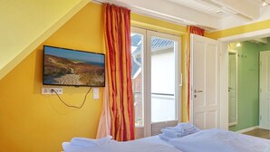 A bedroom with a bed, a TV mounted on the wall, and a view of the outside through a sliding door. - Haus Silvana, App. 6 - 2-raum Appartement mit ca. 50m ² Nutzfläche im Obergeschoss (Wenningstedt-Braderup (Sylt))