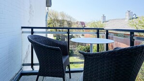 A balcony with wicker furniture and a small table, overlooking a residential area with houses and trees. - Haus Silvana, App. 6 - 2-raum Appartement mit ca. 50m ² Nutzfläche im Obergeschoss (Wenningstedt-Braderup (Sylt))