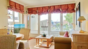 Ein gemütliches Wohnzimmer mit Korbmöbeln, einem Holztisch und Blick ins Freie.