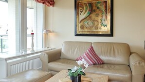 Ein Wohnzimmer mit einem beigefarbenen Sofa, einem Couchtisch aus Holz mit einer Pflanze und einem Fenster mit Blick.