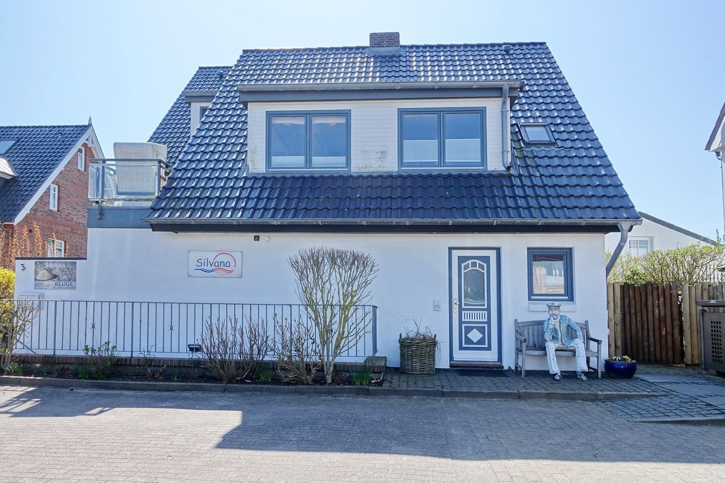 Een woonhuis met twee verdiepingen, een pannendak, een voordeur en een klein portaal met een bankje.