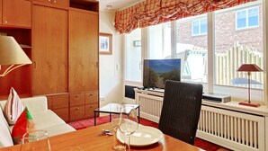 A cozy living room with a dining area, wooden furniture, a television, and a view of the outside. - Haus Silvana, App. 3 - 1-raum Appartement mit ca. 25m ² Nutzfläche im Erdgeschoss (Wenningstedt-Braderup (Sylt))