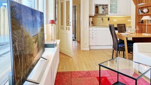A modern kitchen with white cabinets, a dining area with a glass table, and a large painting on the wall. - Haus Silvana, App. 3 - 1-raum Appartement mit ca. 25m ² Nutzfläche im Erdgeschoss (Wenningstedt-Braderup (Sylt))