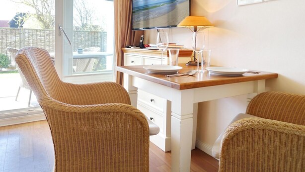 Een kamer met een eettafel, twee rieten stoelen, een televisie en een lamp.