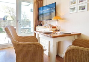 Una habitación con una mesa de comedor, dos sillas de mimbre, un televisor y una lámpara.