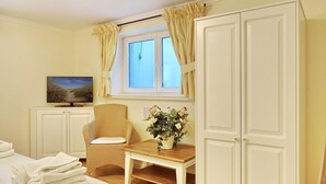 Een hotelkamer met een bed, een stoel, een klein tafeltje met een bloemenvaas, een televisie en een garderobe.