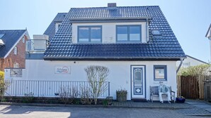 Een woonhuis met twee verdiepingen, een pannendak, een voordeur en een klein portaal met een bankje.