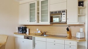 Een compacte keuken met witte kastjes, een ingebouwde magnetron, een koffiezetapparaat en een broodrooster.