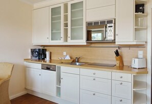 A compact kitchen with white cabinetry, a built-in microwave, a coffee maker, and a toaster. - Haus Silvana, App. 2 - 2-raum Appartement mit ca. 35m ² Nutzfläche im Erd- und Untergeschoss (Wenningstedt-Braderup (Sylt))
