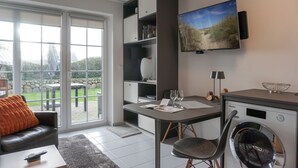 A modern living room with a dining area, a washing machine, and a TV mounted on the wall. - Am Kurpark, App. 3 - 2-raum-appartement im Erd- und UG mit ca. 53m² Nutzfläche für Max. Zwei (Wenningstedt-Braderup (Sylt))