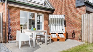 A patio with a table and chairs, a wooden deck chair, and a brick wall. - Am Kurpark, App. 3 - 2-raum-appartement im Erd- und UG mit ca. 53m² Nutzfläche für Max. Zwei (Wenningstedt-Braderup (Sylt))