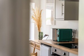 Une cuisine équipée d’un four à micro-ondes, un vase vert contenant des plumes d’herbe des pampas et une chaise en bois.