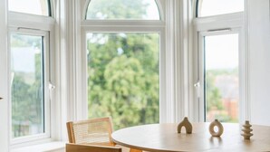 Une pièce avec une table ronde, une chaise et une vue sur la verdure grâce à de grandes fenêtres.