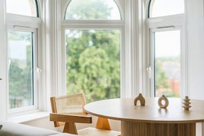 Una habitación con una mesa redonda, una silla y vistas al verdor a través de amplios ventanales.