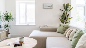Un salon moderne avec un canapé beige, une table basse sur laquelle se trouvent une tasse et des verres, et deux plantes en pot.