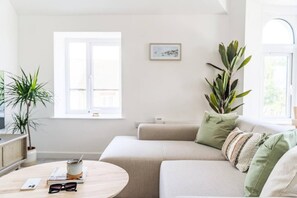 Ett modernt vardagsrum med en beige soffa, ett soffbord med en kopp och glas, och två krukväxter.