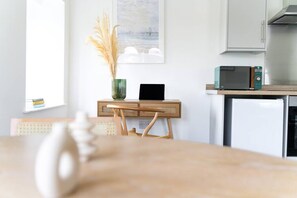 A kitchen with a microwave, a small refrigerator, a wooden desk with a laptop, and a vase with dried plants.