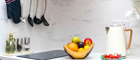 A kitchen with a marble backsplash, a fruit bowl, a coffee maker, and various kitchen utensils.
