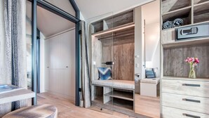 Un dormitorio moderno con armario de vidrio, suelo de madera y mesita de noche con lámpara.