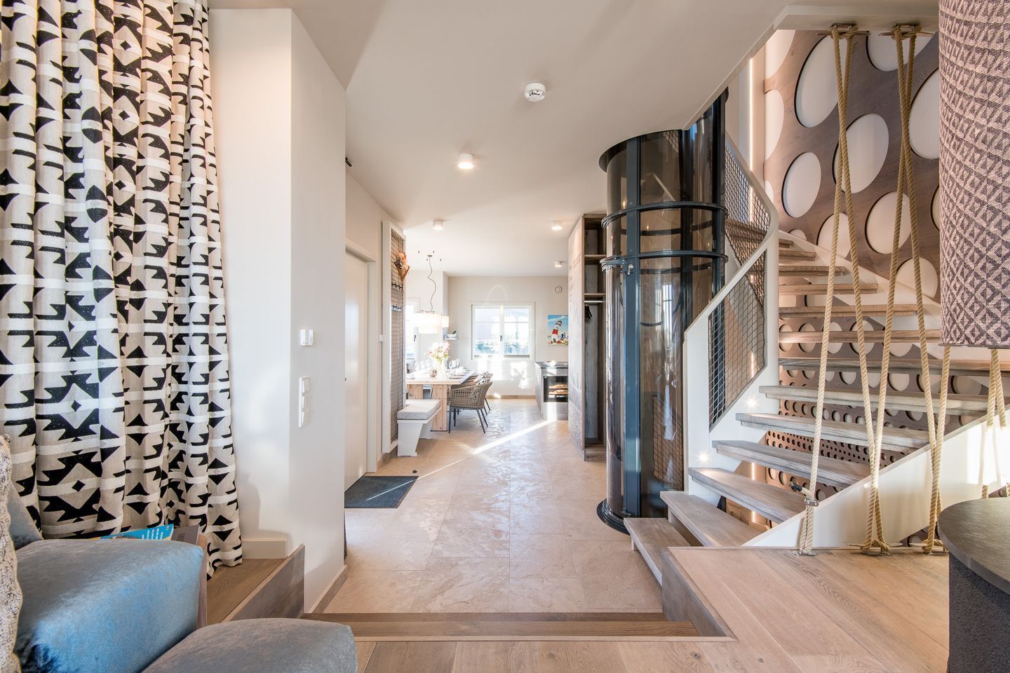 A spacious hallway with a modern staircase, a dining area, and a living space with patterned curtains.
