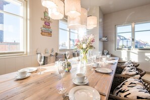 Un coin repas avec une table en bois dressée pour le repas, de grandes fenêtres et une vue sur la ville.