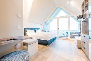 Une chambre à coucher moderne, avec un lit, une table de chevet et une vue sur la mer par une grande fenêtre.