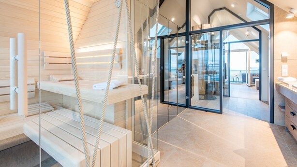 Une salle de spa moderne avec un mur en verre, des sièges en bois et une vue sur l’intérieur.