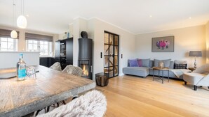 A modern living room with a fireplace, a dining area with a wooden table, and a sofa set. - Strandhaus - Hausteil im Eg,ug,og,dg ca. 157qm Nutzfl., Nichtraucher, Haustiere Nicht Erlaubt (Wenningstedt-Braderup (Sylt))